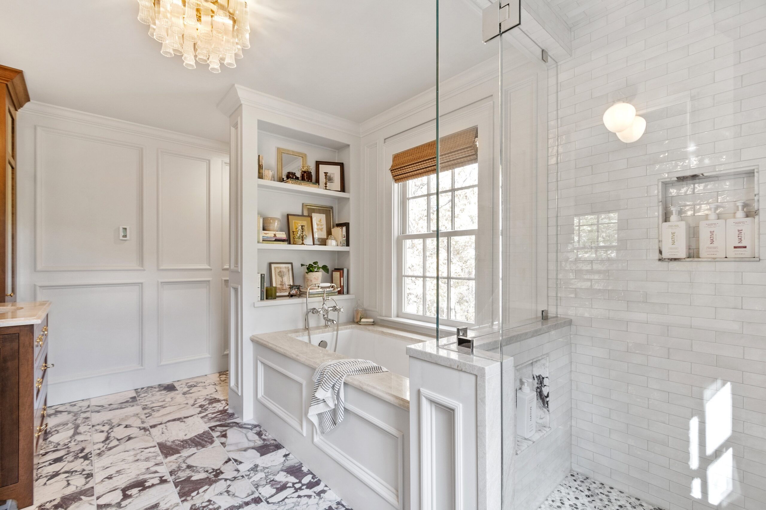 Renovated primary bathroom with marble floor tile, freestanding tub, and glass shower in Medford, MA